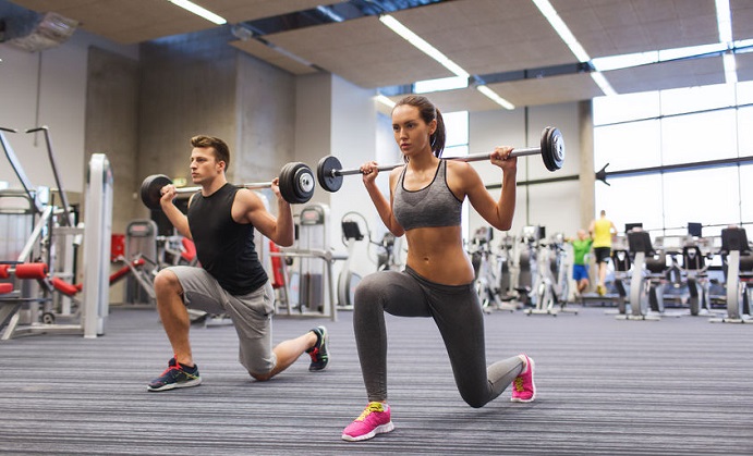 sport, bodybuilding, lifestyle and people concept - young man and woman with barbell flexing muscles and making shoulder press lunge in gym