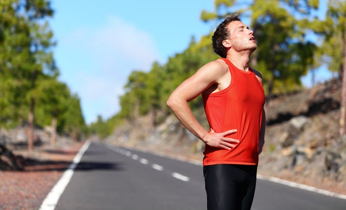 runner resting tired and exhausted after running. jogging man taking a break during training outdoors in on mountain road. young caucasian male fitness model after work out.