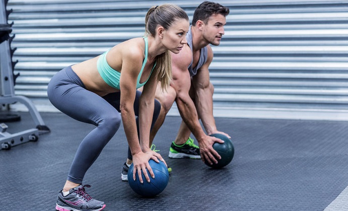 squatting muscular couple doing ball exercise